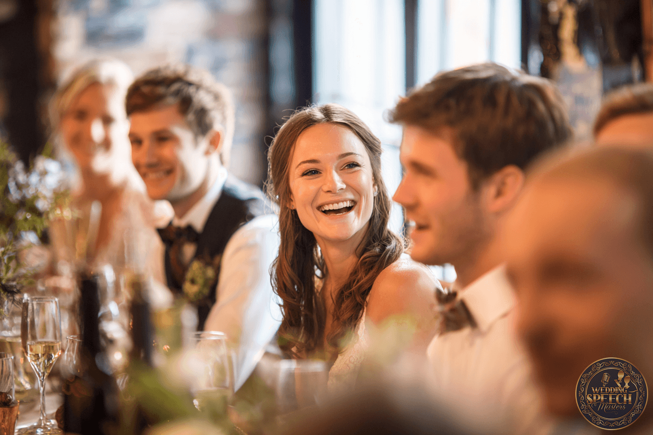 A group of people dressed formally sit at a decorated table, smiling and talking in a warmly lit setting.