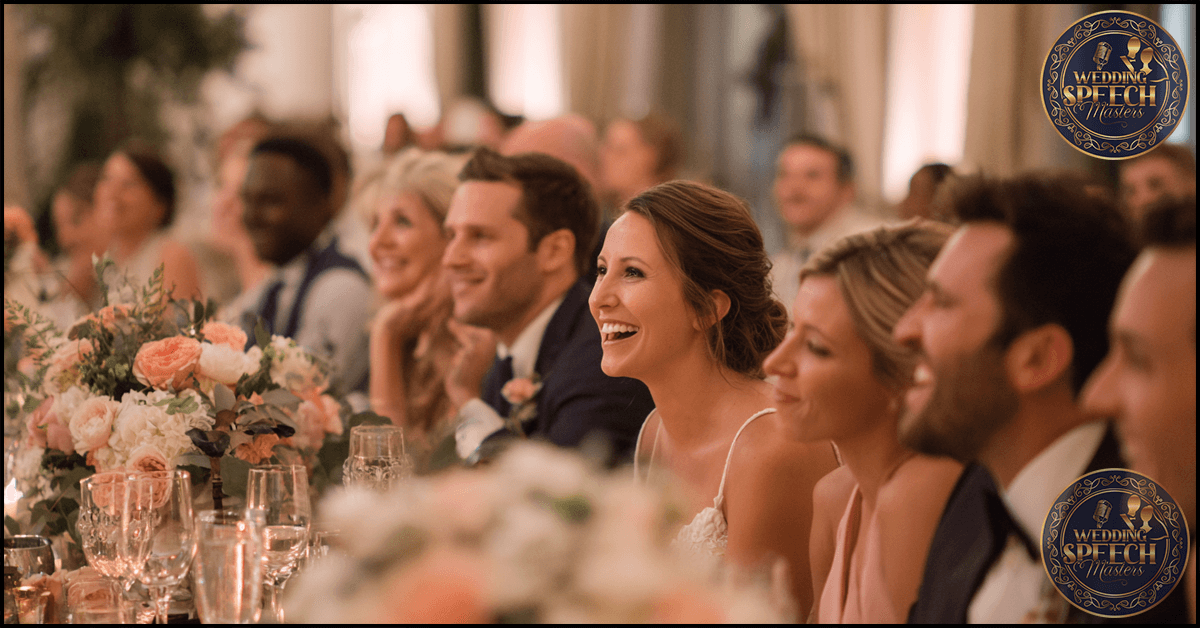 Guests in formal attire sit at a decorated table, smiling and laughing during a wedding reception. Floral arrangements and glassware are visible as the Step Father of the Groom Speech Guide helps create memorable moments.