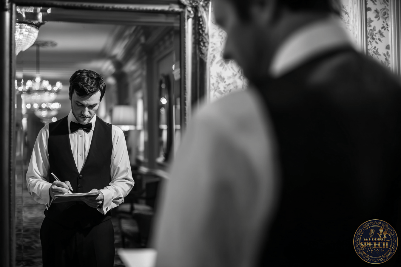 A man in formal attire writes on a notepad, his reflection captured in a large ornate mirror within an elegant, well-lit room-an image that perfectly reflects the professionalism and ethos of our About Us page.